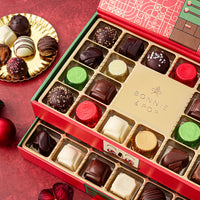 This Christmas Chocolate Truffle Gift Box open to reveal a variety of gourmet chocolate truffles inside. The box is red with green accents and has a decorative design.