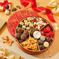 A festive red and gold circular box of assorted gourmet sweets including chocolate covered treats, nut clusters, and candy balls.