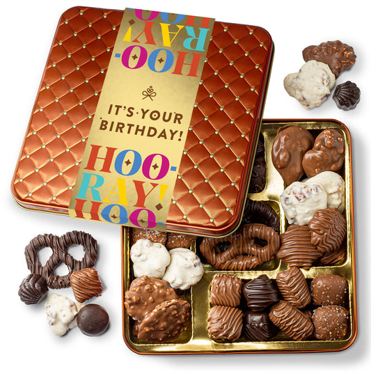 A collection of assorted chocolates presented in a square tin container with a birthday greeting on the lid.
