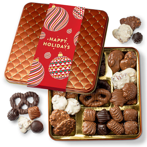 A variety of chocolates with different textures and finishes, presented in a gold tin with a festive red 'Happy Holidays' lid. The chocolates appear to include milk and dark varieties, possibly with holiday-themed decorations and flavors.